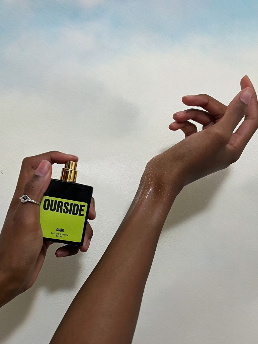 two hands spraying perfume onto a wrist on a sky background